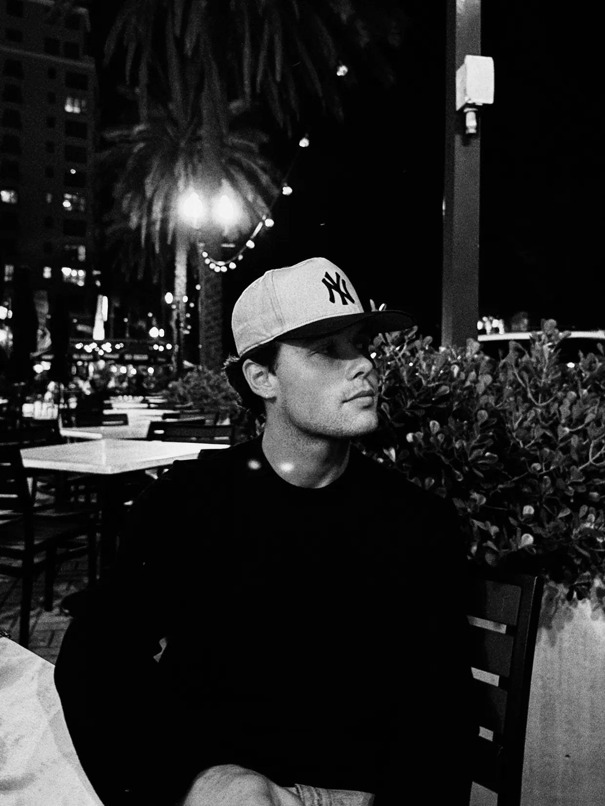 Gavin Frantz in a Yankees cap, seated at an outdoor table at night under string lights