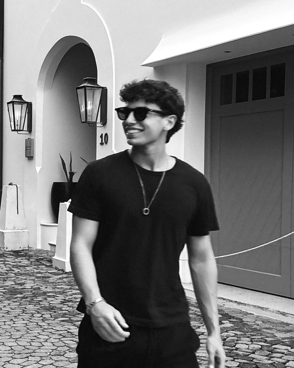 Smith Rice, in sunglasses and a black tee, smiling on a cobblestone street